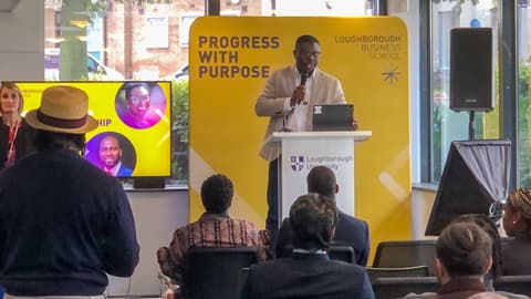 A speaker on stage as part of the Black Excellence UK event at Loughborough Business School.