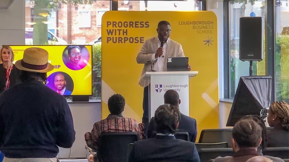 A speaker on stage as part of the Black Excellence UK event at Loughborough Business School.