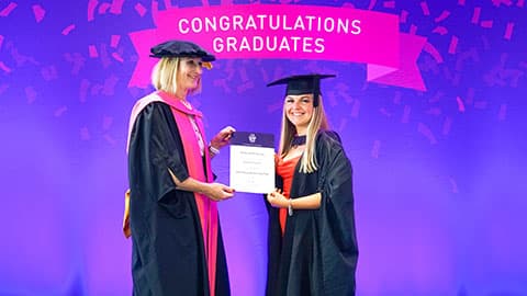 Brooke Yasmin Norcross on stage with their certificate from Professor Jan Godsell.