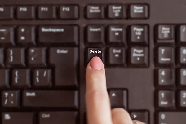 A person's finger pressing the delete button on a keyboard.