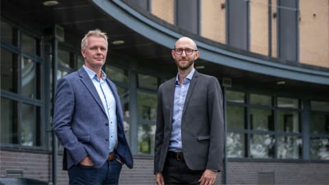 Professors Tom Jackson and Ian Hodgkinson stand in front of the Loughborough Business School building.