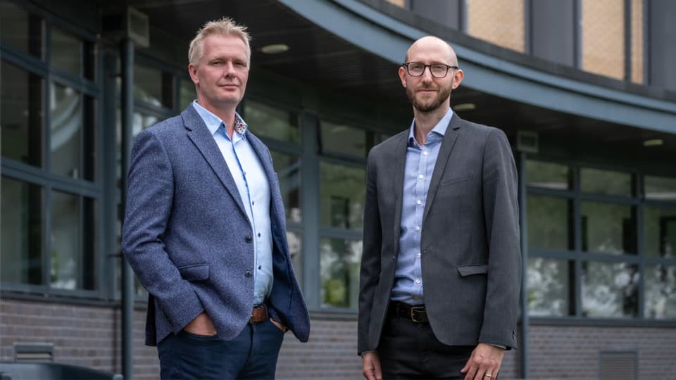 Professors Tom Jackson and Ian Hodgkinson stand in front of the Loughborough Business School building.