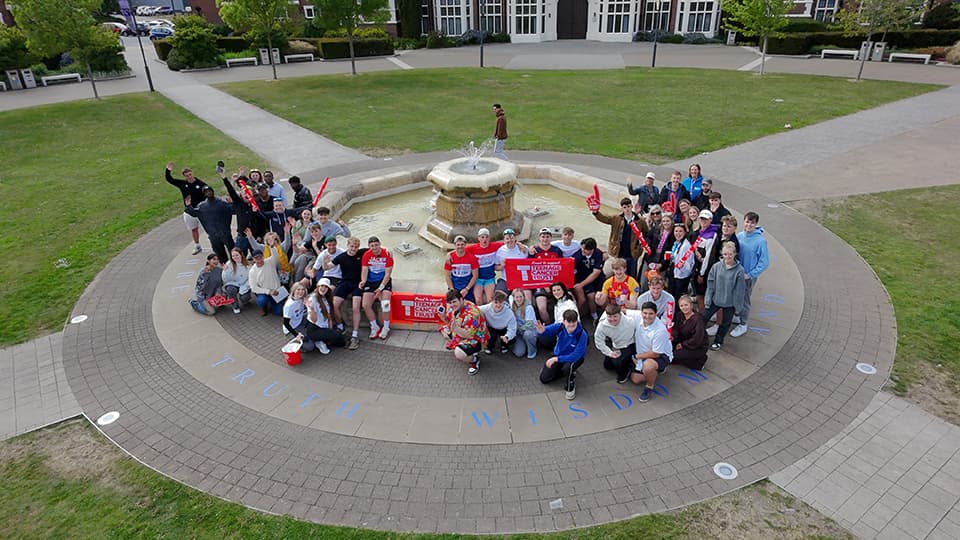 A large group of students gathered around the Hazlerigg fountain on the Loughborough University campus.