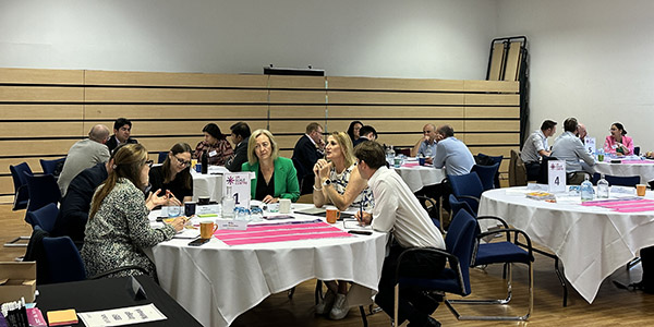 People seated at round tables during a conference, with materials and table numbers visible.