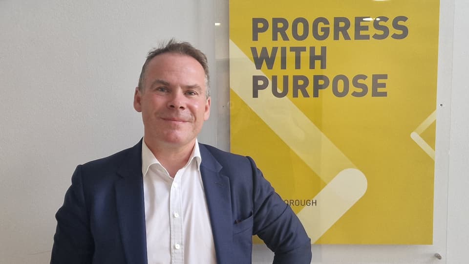 Ian McLernon standing next to a yellow poster that says 'progress with purpose'.
