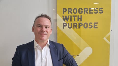 Ian McLernon standing next to a yellow poster that says 'progress with purpose'.