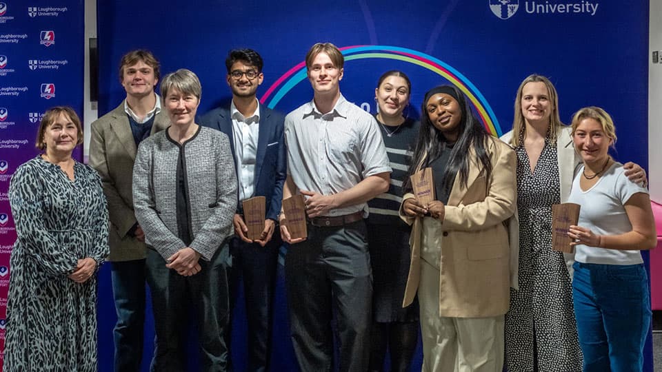A group of staff and students standing in front of a banner.
