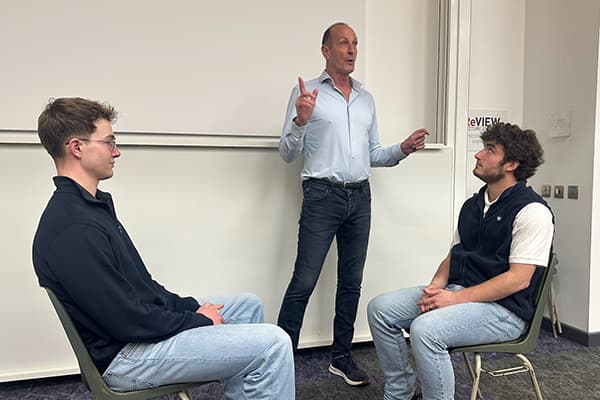 Two students sat opposite each other, with Floyd Woodrow talking behind them.
