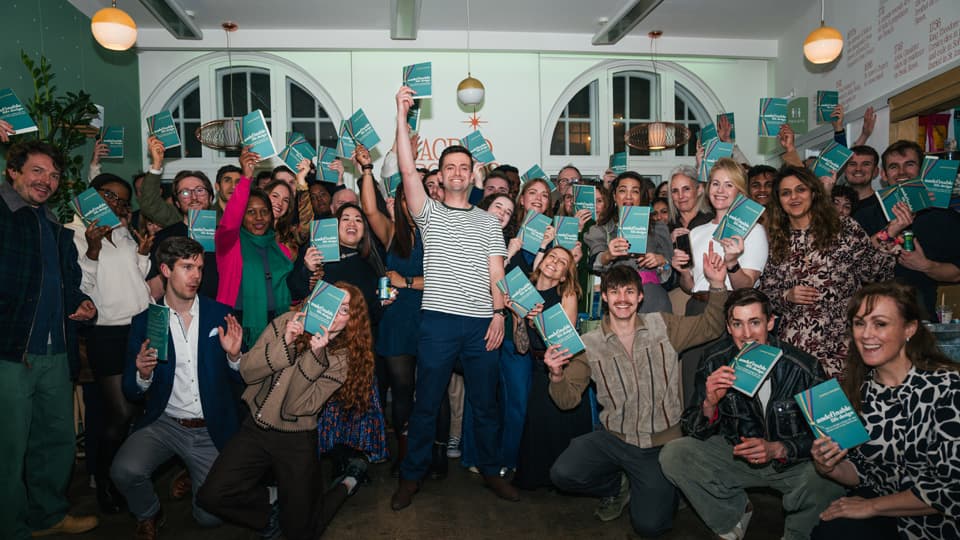 Alum Charlie Rogers with a large group of people holding his new book at a launch event.