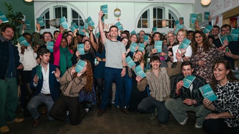 Alum Charlie Rogers with a large group of people holding his new book at a launch event.