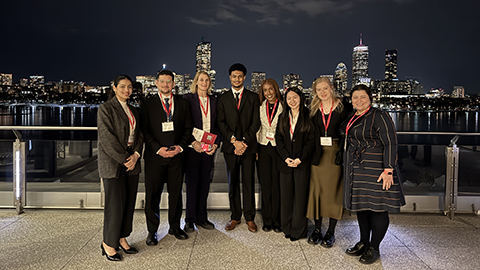 UK SCALE students and staff posing together at an evening event in Boston, with the city skyline visible in the background