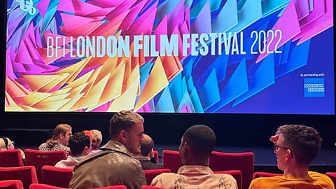 People sitting in red chairs in front of a large screen with the text 'BFI London Film Festival 2022'.