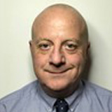 Patrick Baker wearing a grey shirt and dark tie