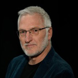 Thomas Blood wearing a dark suit against a black backdrop