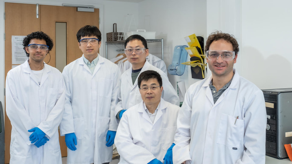 group of male researchers in lab coats and blue gloves smiling