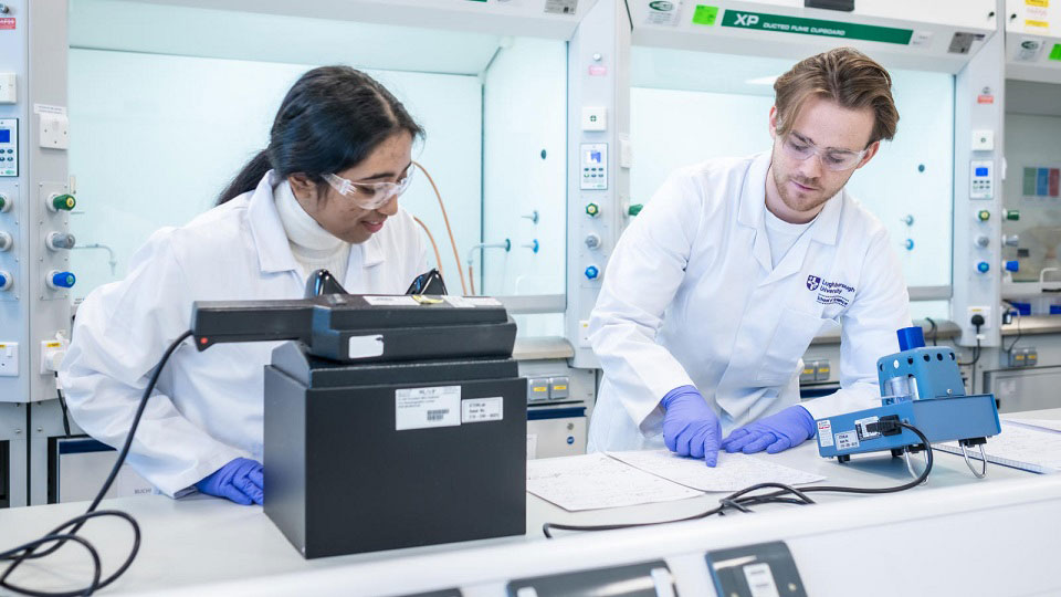 A male and female student in lab gear carrying out experiment