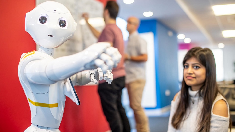 Humanoid robot pepper facing forward with a female student slightly blurred in the background.