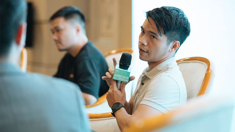 Leo Nguyen sitting at the conference table holding a microphone with the logo of Green Horizon.