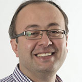 A headshot of Firat Batmaz wearing glasses and a checked shirt