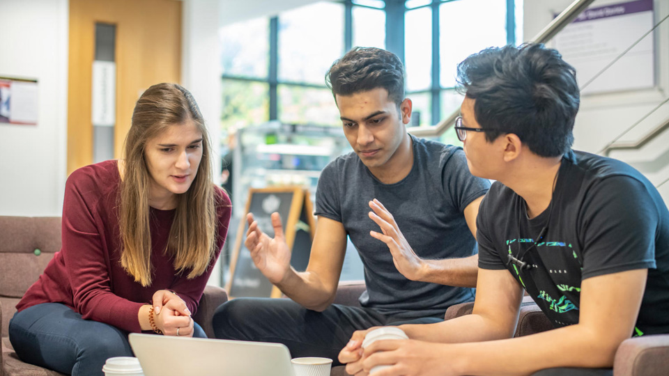 Three students talking around a laptop
