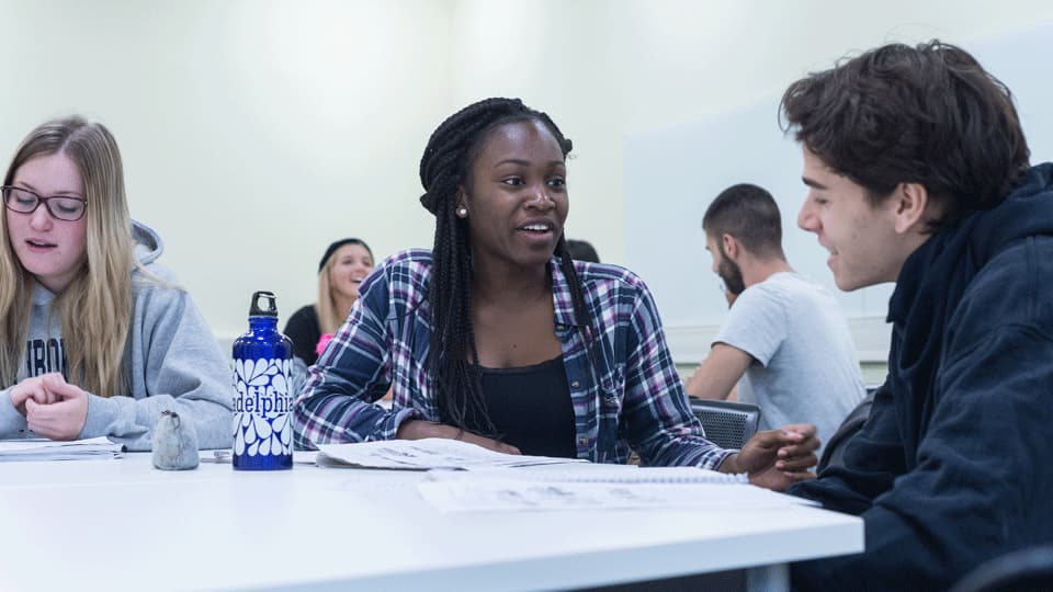 three students have a conversation during a lesson. students in the background
