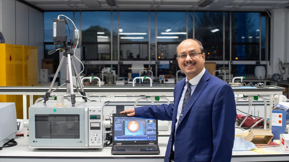 image of academic in lab smiling with hand on laptop