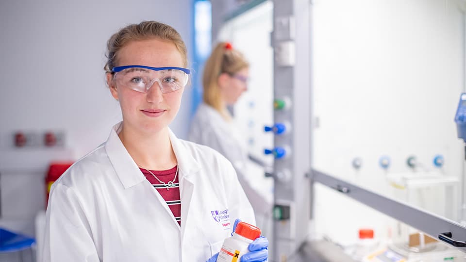 Female student smiling at the camera in lab coat