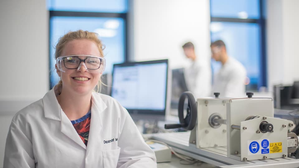 Student in lab coat and goggles smiling