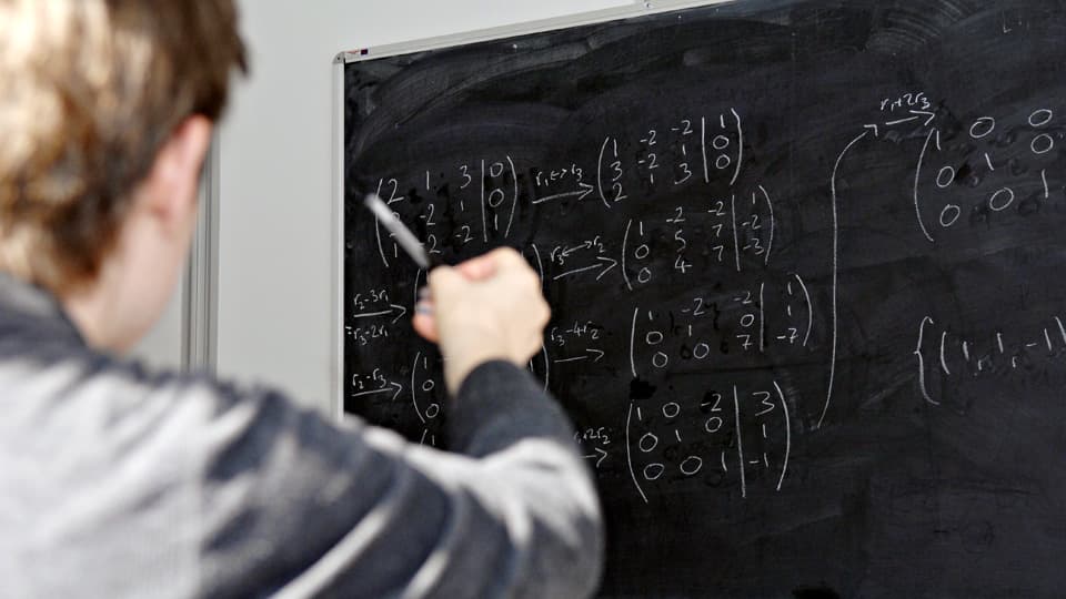 a man standing in front of a blackboard that is covered with mathematical formula
