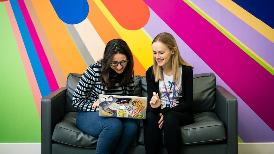 two students sitting on a sofa reading a brochure