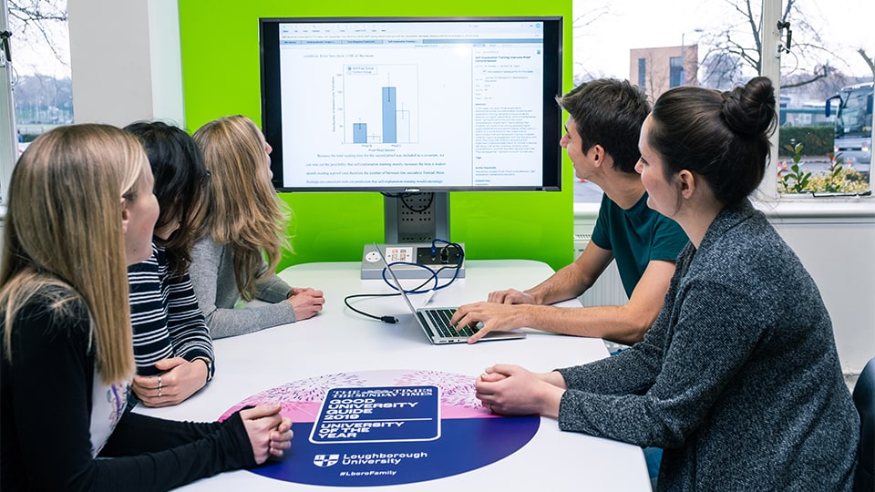 five students sitting around a desk and looking at a computer screen