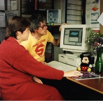 Geoff Simpson and a colleague using a desktop computer, Geoff is wearing a Superman  t-shirt