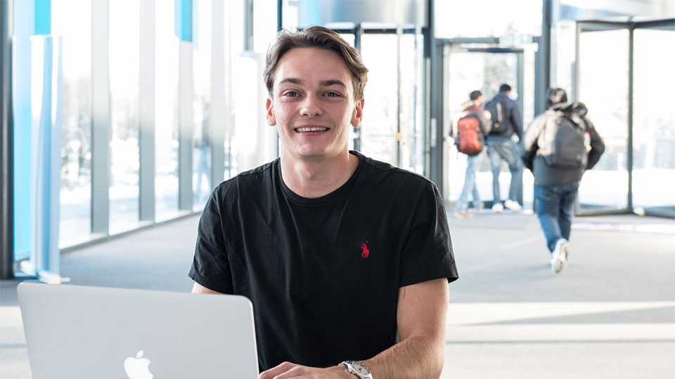 A male student sat in the foyer of the STEMLab at Loughborough University using a laptop.