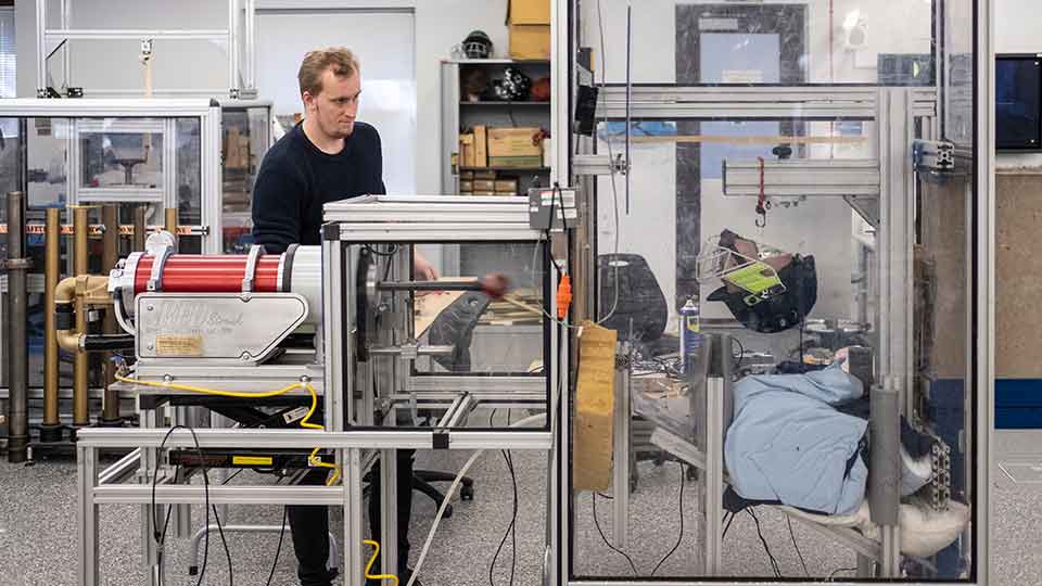 Student in a lab with equipment for testing the impact the ball has on a cricket helmet