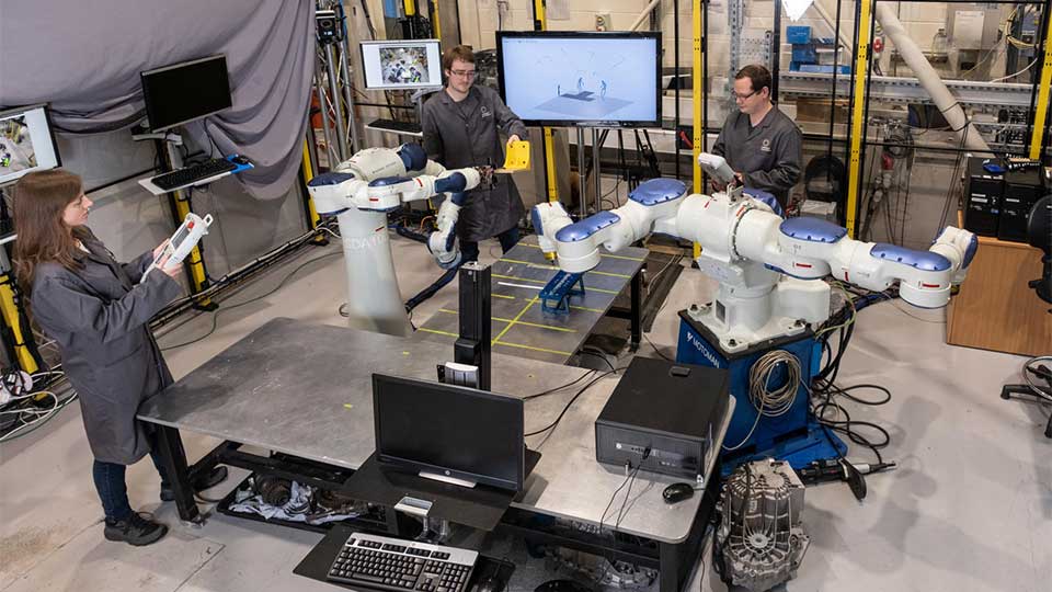 Three technicians in an intelligent automation centre workshop working on a human-robot test cell.