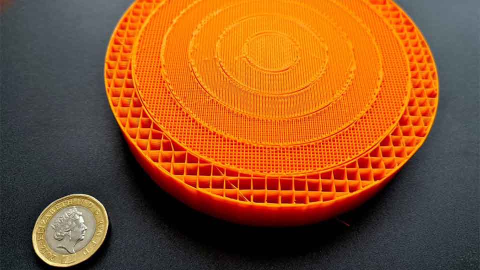 A close-up of an orange 3D-printed prototype which is placed next to a two-pound coin.