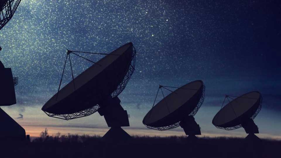 Silhouettes of satellite dishes and radio antennas against a starry night sky.