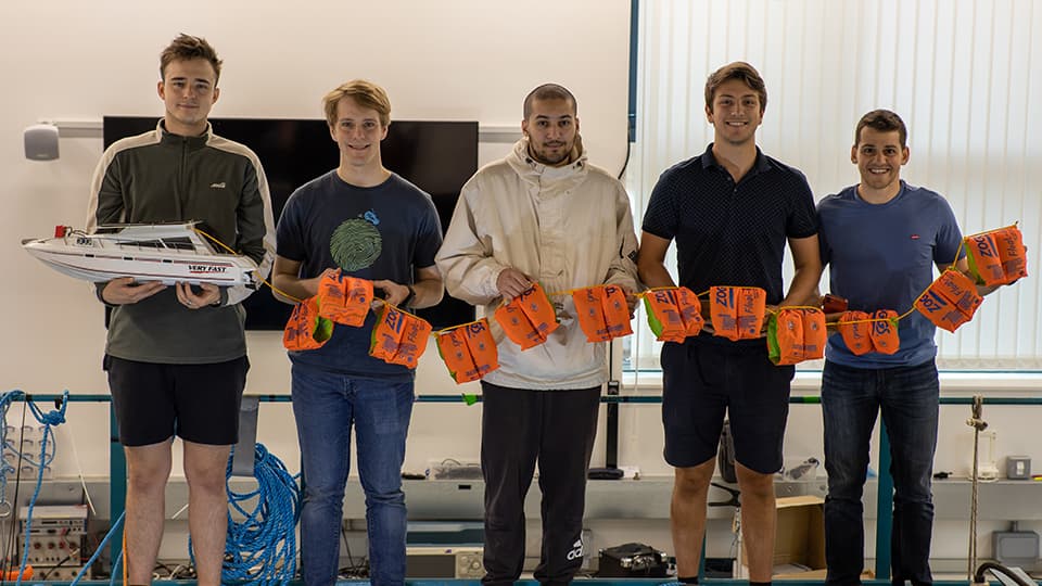 Adam stood with other students holding a boat engineering project