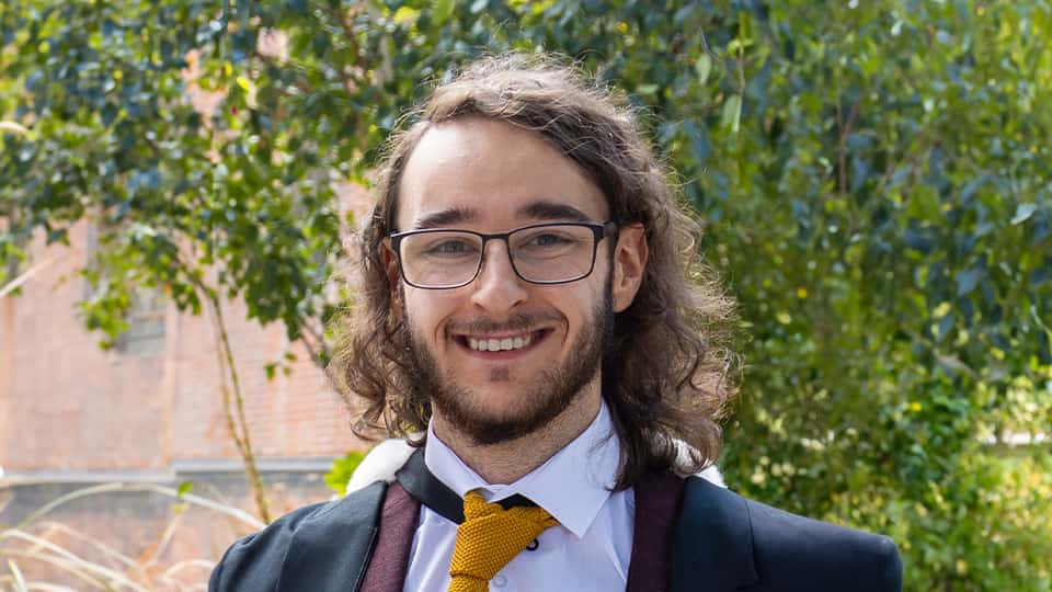 James stood outside by a tree in his graduation gown