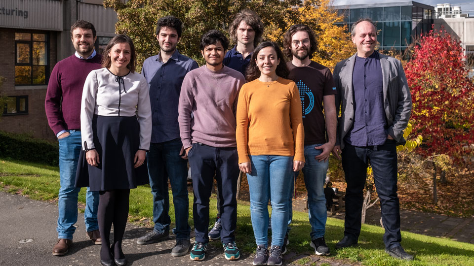 Members of the Emergent Photonics Research Centre standing outside the Physics department building