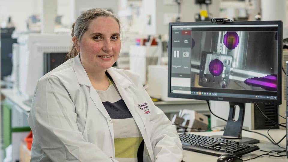 Sarah Bugby sitting at a computer desk in a laboratory