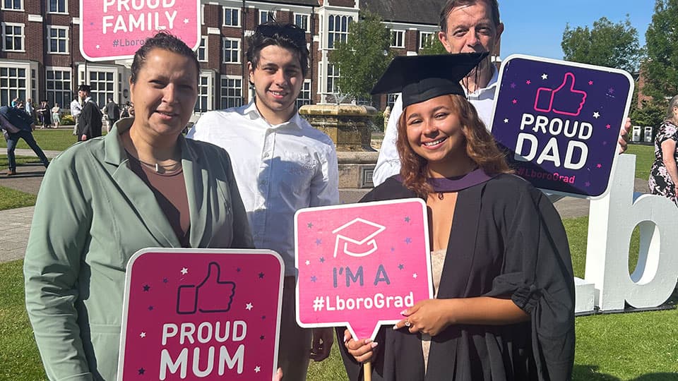 Graduate wearing graduation gown and hat with family holding signs