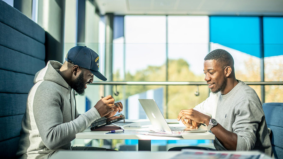 Two students using laptops in breakout space