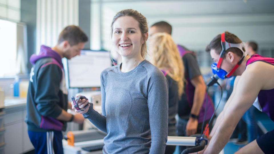 A group of people in a Sport Science lab looking at a computer screen, a man on the bike is being monitored, one woman turns to face the camera.