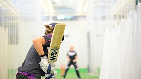 Close up of a cricketer from the back holding a bat about to strike a ball