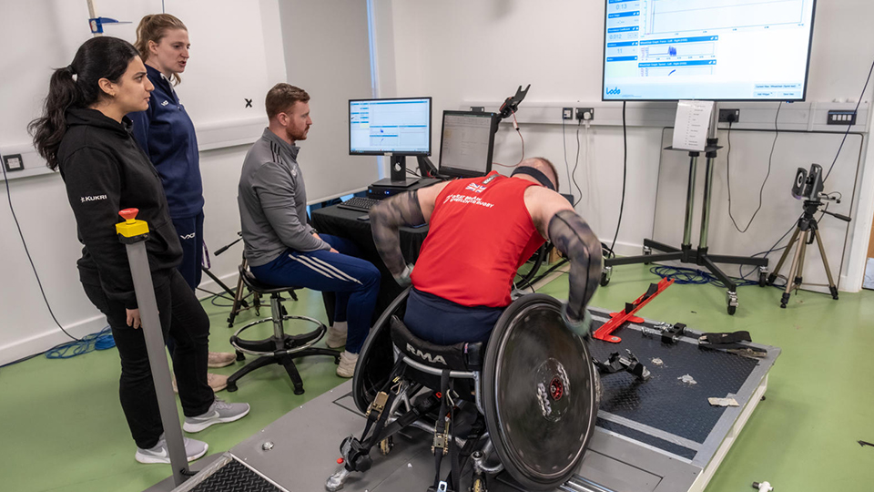 A para athlete in a wheelchair undergoes some testing with three researchers