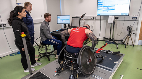 A para athlete in a wheelchair undergoes some testing with three researchers
