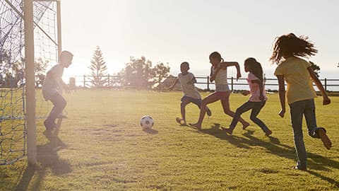 3 children playing footback with sun shining in background