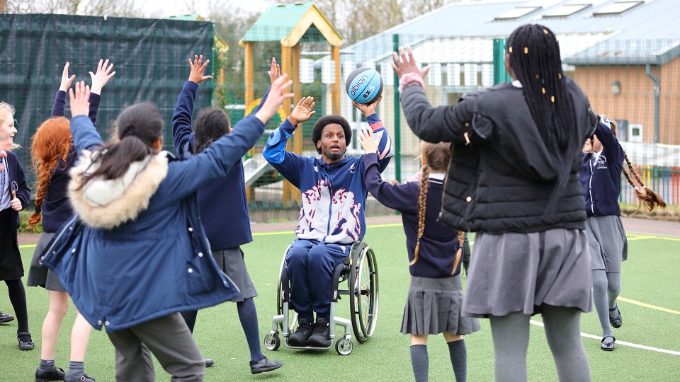 An athlete demonstrates wheelchair basketball to a group of schoolchildren.