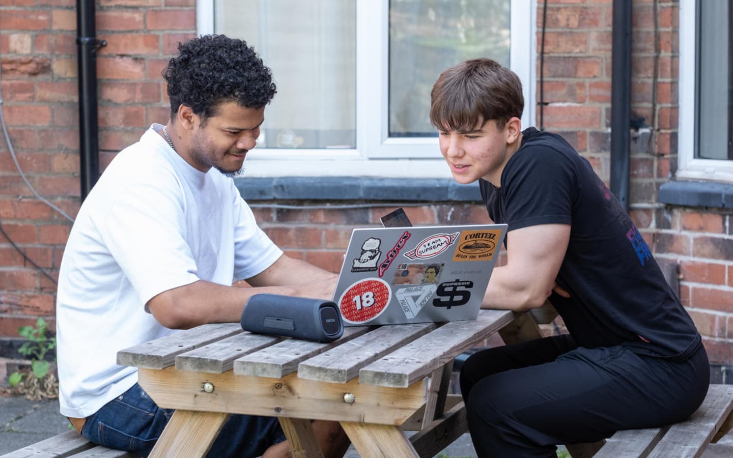 2 students in their off campus garden on their laptop